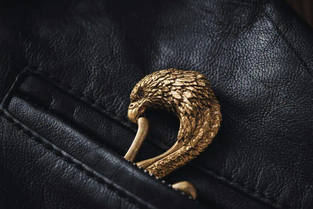Close-up of a golden eagle-shaped brooch placed on black leather, highlighting intricate design details.