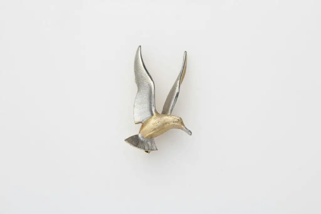 Stylish seagull brooch in silver and gold tones on a clean white background.