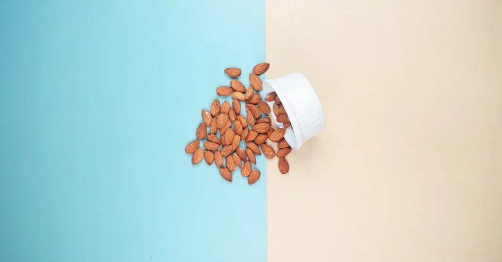 A bowl of almonds spills onto a blue and beige backdrop. Minimalist food concept.