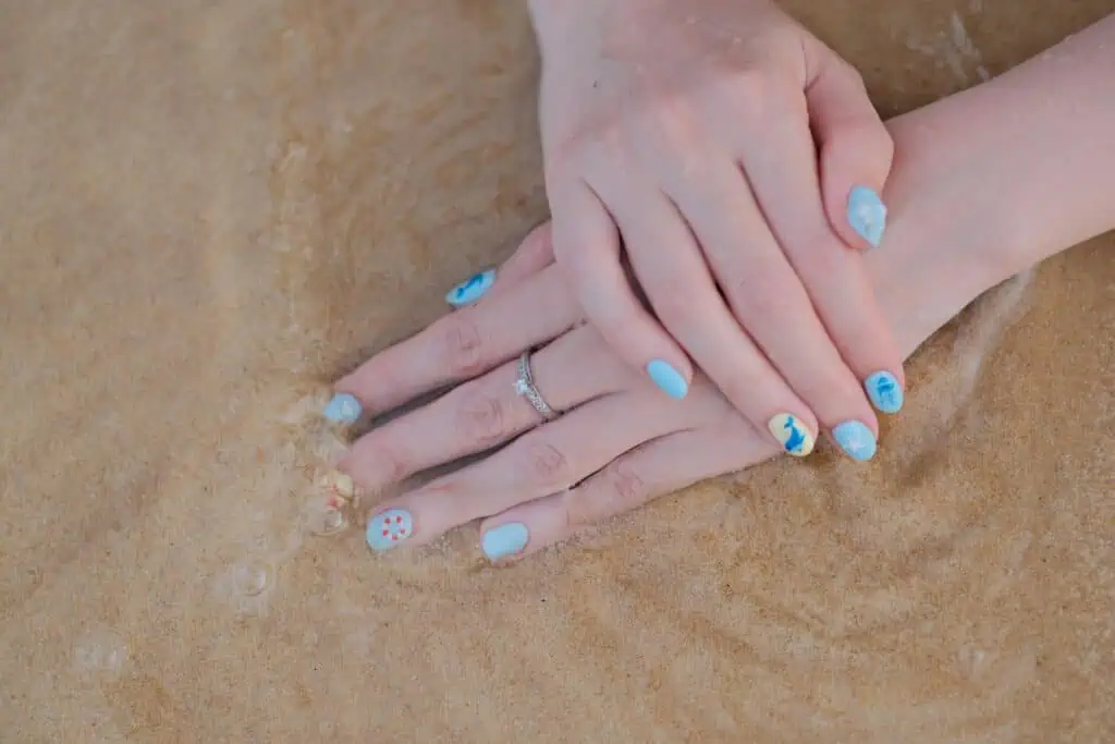 A serene close-up of hands with beach-themed nail art against sandy beach waves.