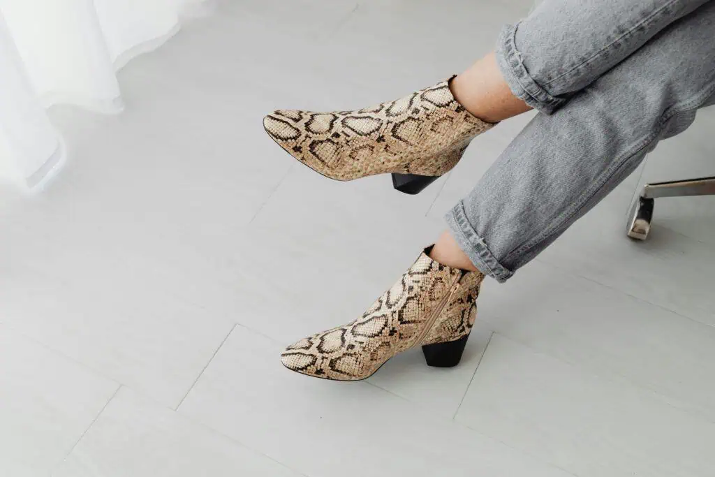 Stylish snake print boots paired with jeans on a light indoor floor.