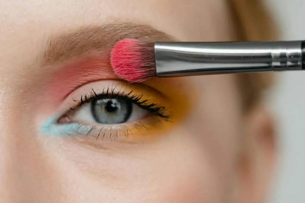 Detailed close-up of eye makeup using vibrant eyeshadow and brush.