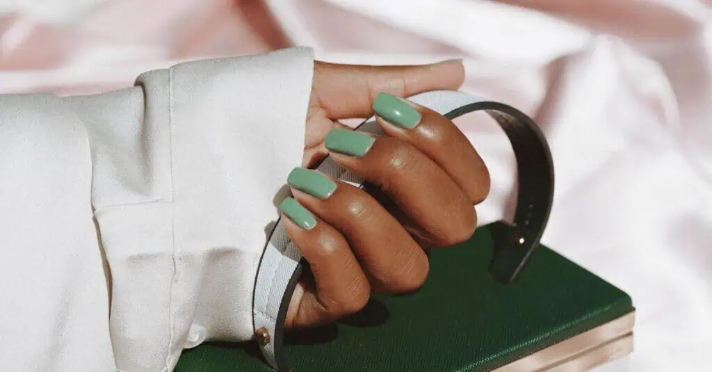 Close-up of a woman's hand with green nails holding a stylish handbag, showcasing fashion and elegance.