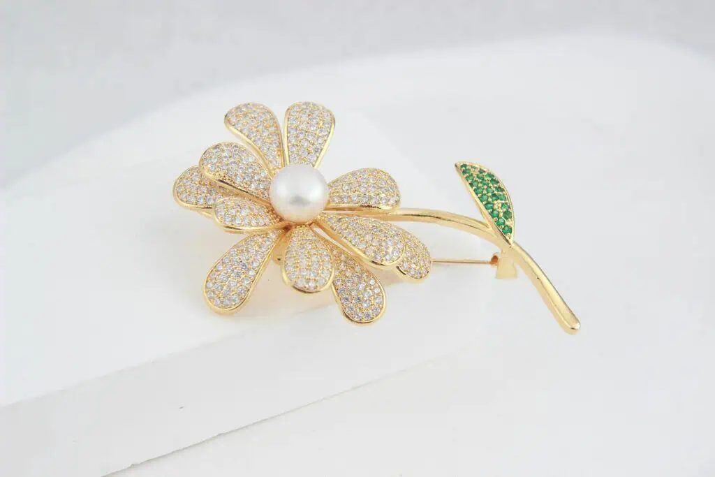 Luxurious gold flower brooch adorned with diamonds and pearls on a white background.