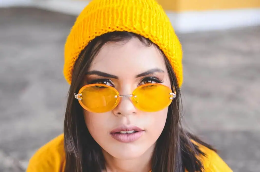 Stylish portrait of a woman wearing a yellow beanie and sunglasses outdoors.