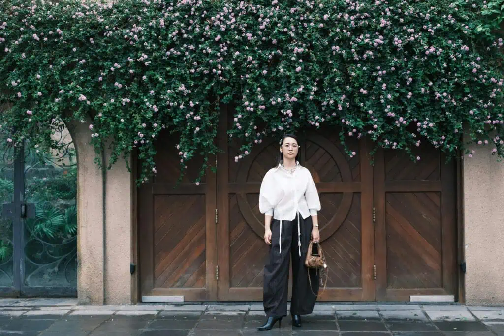 Stylish woman in elegant attire standing before a wooden door adorned with floral vines.