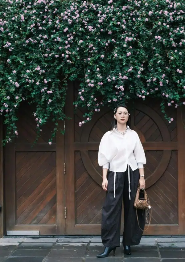 Stylish woman in elegant attire standing before a wooden door adorned with floral vines.