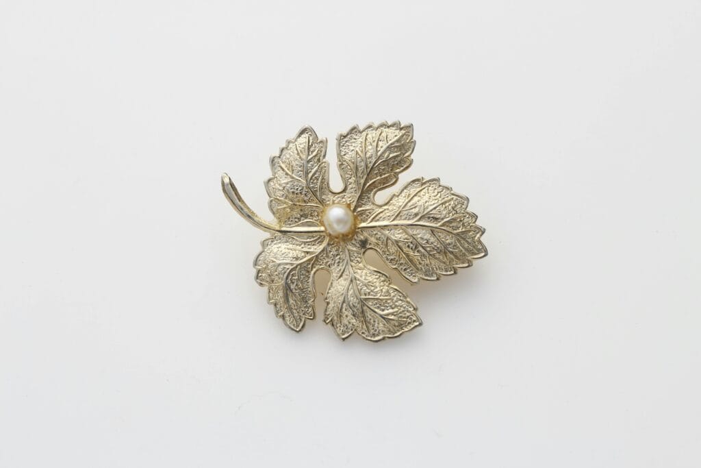 Delicate leaf-shaped brooch featuring a pearl center on a white surface.