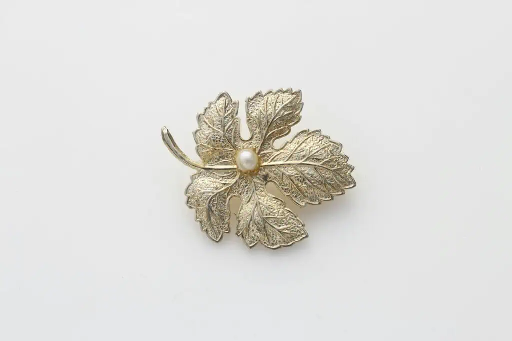 Delicate leaf-shaped brooch featuring a pearl center on a white surface.
