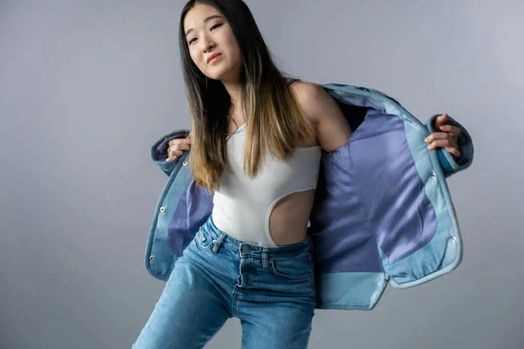 Stylish Asian woman posing in denim and white top against a gray background.