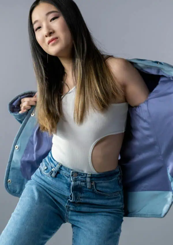 Stylish Asian woman posing in denim and white top against a gray background.