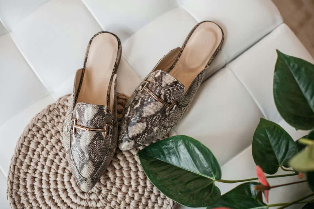 Elegant leather mules in python pattern on a textured beige mat, enhancing women's fashion style.