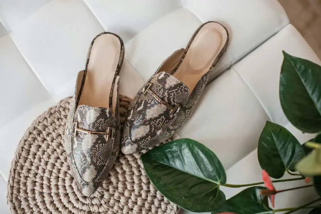 Elegant leather mules in python pattern on a textured beige mat, enhancing women's fashion style.