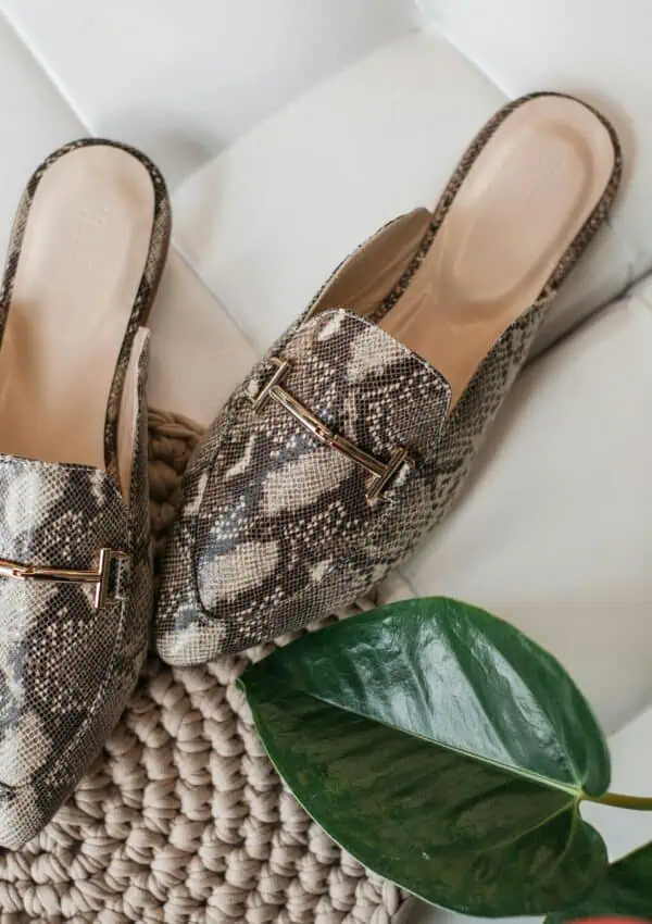 Elegant leather mules in python pattern on a textured beige mat, enhancing women's fashion style.